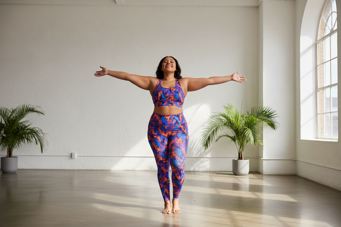 Plus-size woman in bold print activewear standing confidently with arms open wide in a bright studio